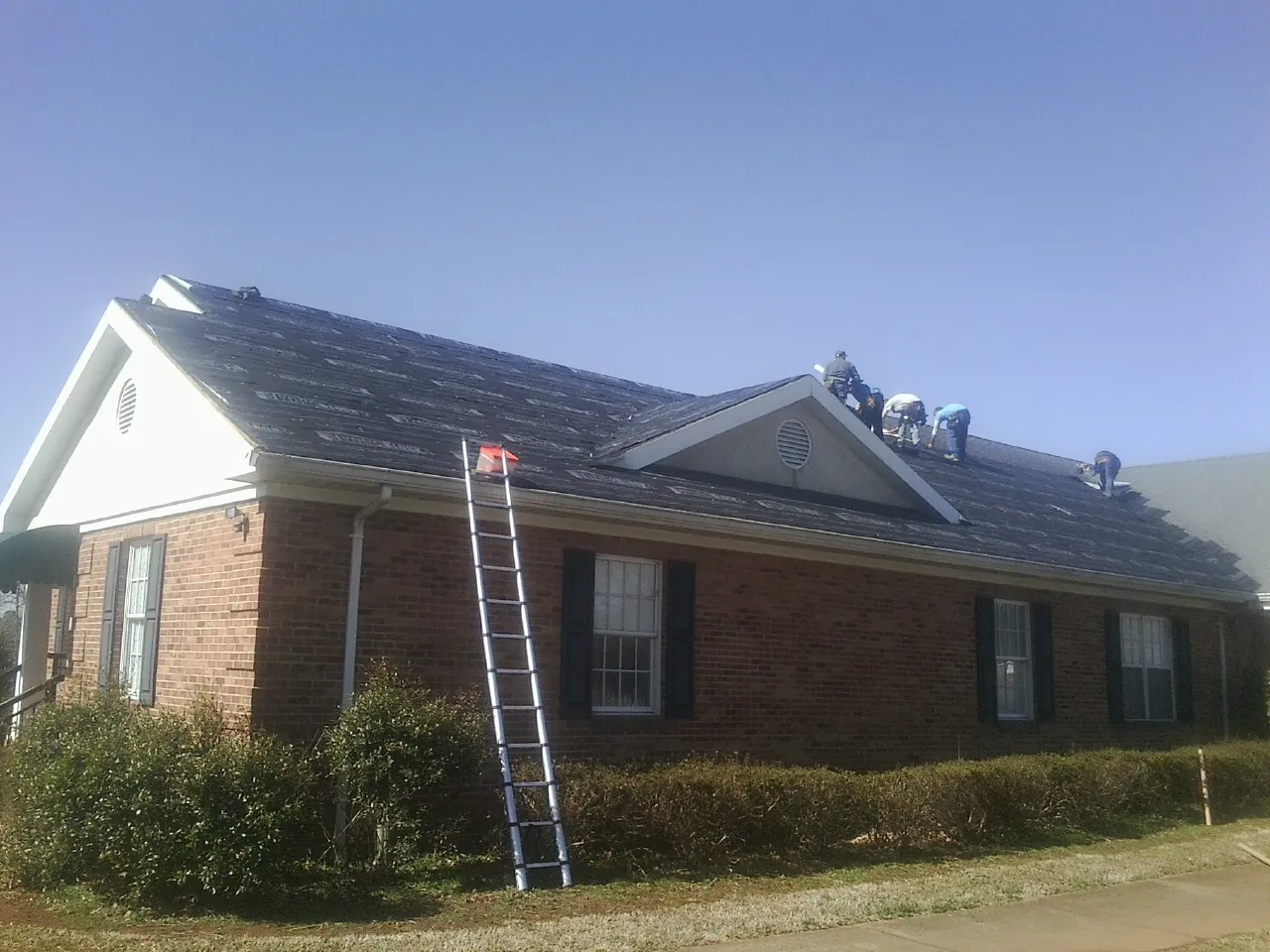 Crew tearing shingles off a brick ranch roof with a ladder set — Emergency Roof Repair work by our crew in Spring Mills