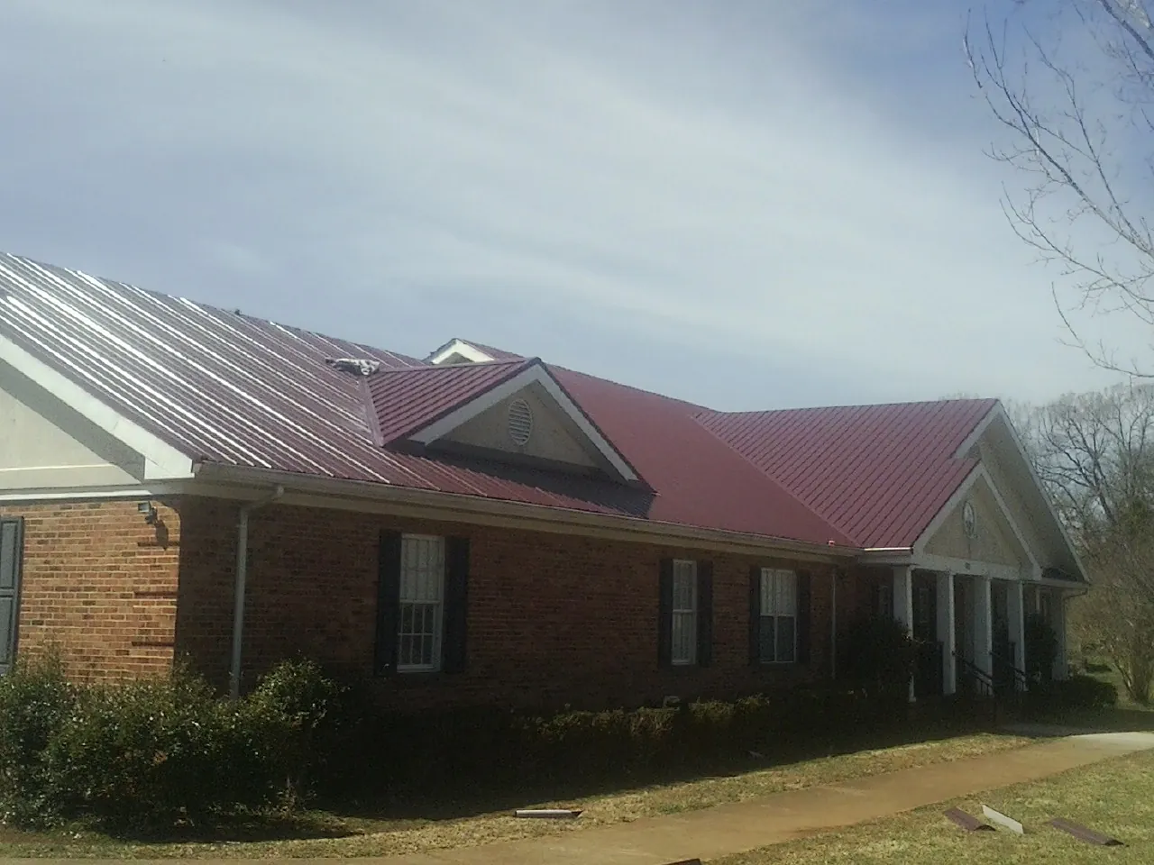 Red metal roof with gabled entries on a long brick building, from a Hail Damage Roof Repair job in Spring Mills
