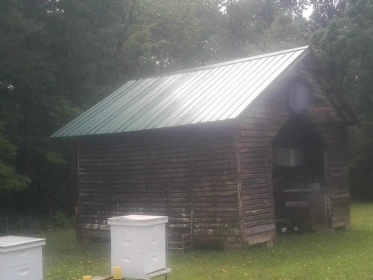 Green metal roof on a weathered barn beside stacked beehives in Spring Mills