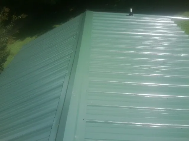 New green metal panels meeting at the ridge of a roof — Flat Roof Repair work by our crew in Spring Mills