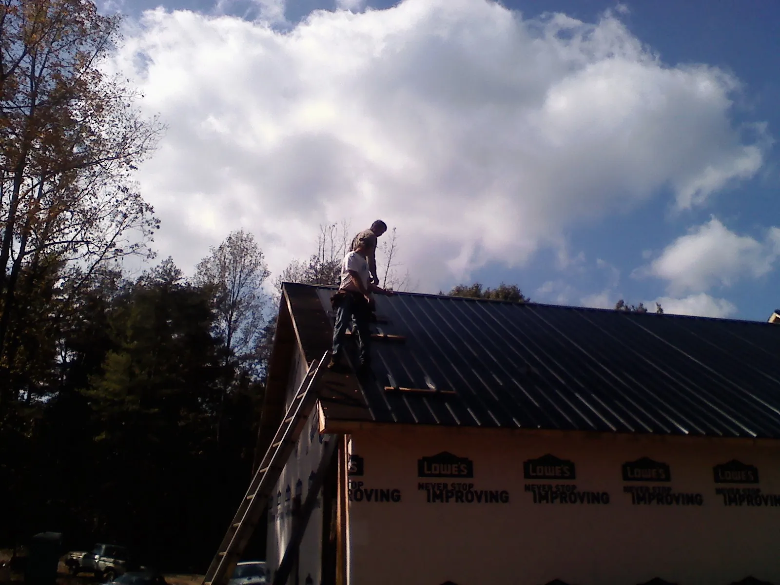 Roofer fastening dark metal panels high against a cloudy sky, from a Roof Inspection job in Spring Mills